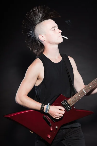 Punkrock-Mann mit roter E-Gitarre und Mohawk-Frisur. Gesichtsausdruck. isoliert auf schwarzem Hintergrund. Studioaufnahme. — Stockfoto