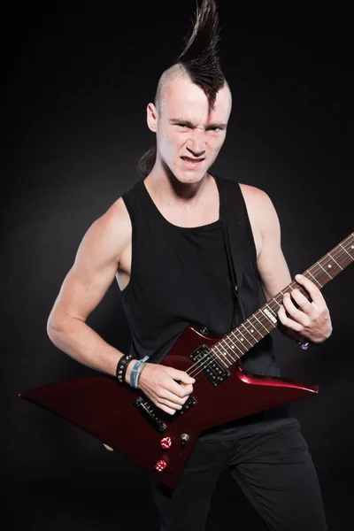 Punk rock hombre con guitarra eléctrica roja y corte de pelo mohawk. Cara expresiva. Aislado sobre fondo negro. Captura de estudio . — Foto de Stock