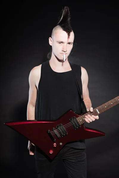 Punk rock avec guitare électrique rouge et coupe de cheveux mohawk. Visage expressif. Isolé sur fond noir. Plan studio . — Photo