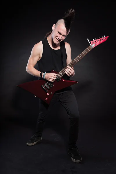 Punk rock homem com guitarra elétrica vermelha e corte de cabelo mohawk. Cara expressiva. Isolado em fundo preto. Estúdio . — Fotografia de Stock