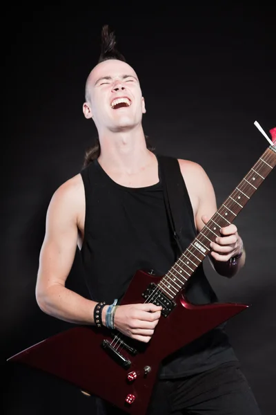 Uomo punk rock con chitarra elettrica rossa e taglio di capelli mohawk. Faccia espressiva. Isolato su sfondo nero. Studio girato . — Foto Stock
