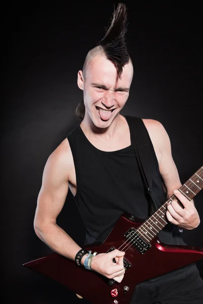 Punk rock homem com guitarra elétrica vermelha e corte de cabelo mohawk. Cara expressiva. Isolado em fundo preto. Estúdio . — Fotografia de Stock