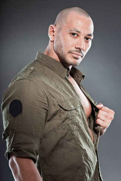 Muscled tough guy wearing green army shirt. Good looking man. Isolated on grey background. Studio shot. Healthy. Fitness.