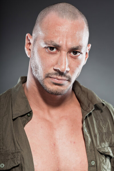 Muscled tough guy wearing green army shirt. Good looking man. Isolated on grey background. Studio shot. Healthy. Fitness.