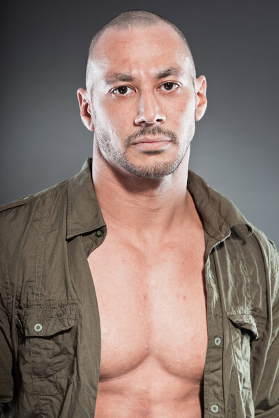 Muscled tough guy wearing green army shirt. Good looking man. Isolated on grey background. Studio shot. Healthy. Fitness.