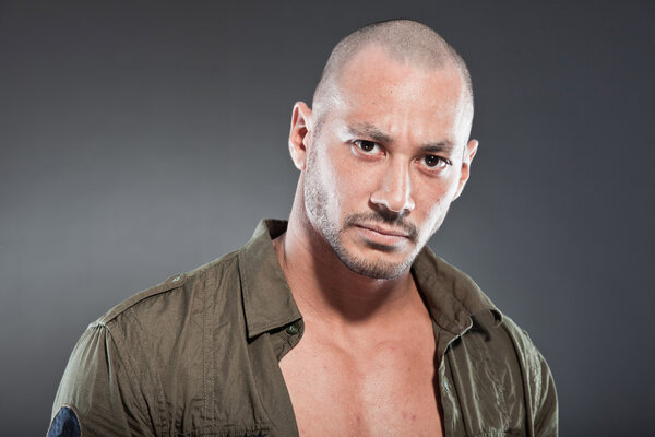 Muscled tough guy wearing green army shirt. Good looking man. Isolated on grey background. Studio shot. Healthy. Fitness.