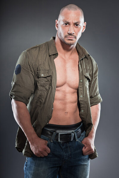 Muscled tough guy wearing green army shirt. Good looking man. Isolated on grey background. Studio shot. Healthy. Fitness.