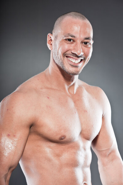 Shirtless muscled fitness man. Cool looking. Tough guy. Brown eyes. Bald. Tanned skin. Studio shot isolated on grey background.