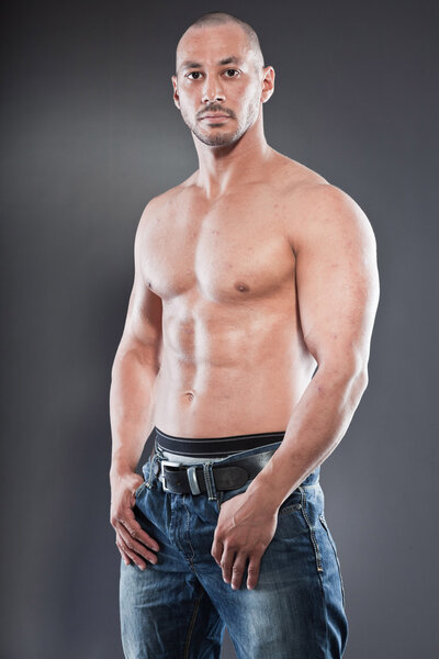 Shirtless muscled fitness man. Cool looking. Tough guy. Brown eyes. Bald. Tanned skin. Studio shot isolated on grey background.