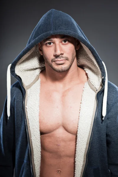 Muscled fitness man. Cool looking. Tough guy. Brown eyes. Bald. Wearing blue hoody shirt. Tanned skin. Studio shot isolated on grey background. — Stock Photo, Image