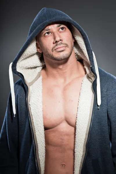 Hombre musculoso de fitness. Bonito aspecto. Un tipo duro. Ojos marrones. Calvo. Llevando camisa azul con capucha. Piel bronceada. Estudio plano aislado sobre fondo gris . — Foto de Stock