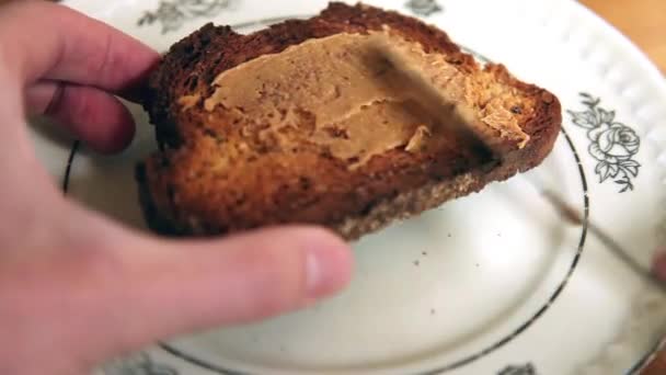 Toastový chléb, šíří se peanutbutter v kuchyni. mužské ruky hospodářství chléb. — Stock video