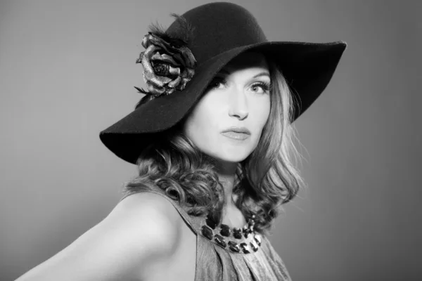 Glamour vintage svartvita porträtt av vacker kvinna med långt hår. klädd i svart hatt med blomma. Studio porträtt isolerad på grå. — Stockfoto