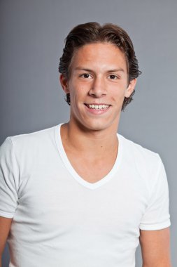 kahverengi saçlı ve gözlü genç çocuk. Beyaz tişört giyiyor. Çekici. rahat kıyafet. ifadeler. gri arka plan üzerinde izole stüdyo portre portre.