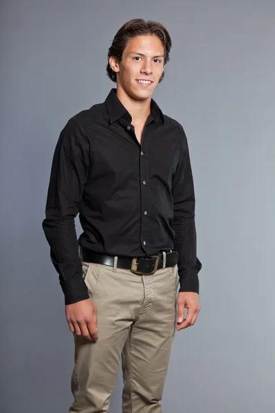 Adolescente con cabello castaño y ojos. Con camisa negra y pantalones caqui. Muy guapo. Ropa casual. Expresiones. Retrato de estudio aislado sobre fondo gris . — Foto de Stock