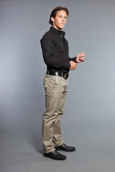 Ragazzo con i capelli castani e gli occhi. Indossava camicia nera e pantaloni kaki. Bell'aspetto. Abbigliamento casual. Espressioni. Studio ritratto isolato su sfondo grigio . — Foto Stock