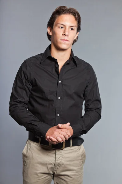 Adolescente con cabello castaño y ojos. Con camisa negra y pantalones caki. Muy guapo. Ropa casual. Expresiones. Retrato de estudio aislado sobre fondo gris . — Foto de Stock