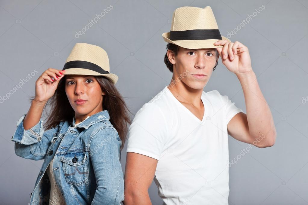 Pretty young couple casual dressed wearing a straw hat. Brother and sister. Good looking. Brown hair and eyes. Studio portrait isolated on grey background.