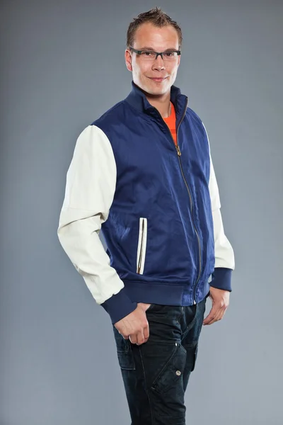 Glücklicher junger Mann mit kurzen Haaren trägt blaue Baseballjacke und blaue Jeans. — Stockfoto