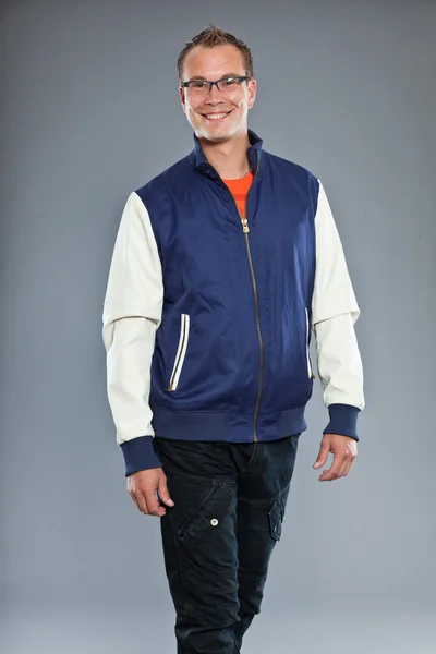 Счастливый молодой человек с короткими волосами в синей бейсбольной куртке и синих джинсах . — стоковое фото