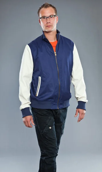 Happy young man with short hair wearing blue baseball jacket and blue jeans. — Stock Photo, Image