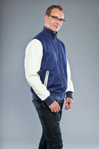 Glücklicher junger Mann mit kurzen Haaren trägt blaue Baseballjacke und blaue Jeans. — Stockfoto