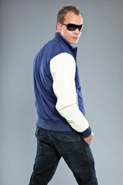 Happy young man with short hair wearing blue baseball jacket and blue jeans. — Stock Photo, Image