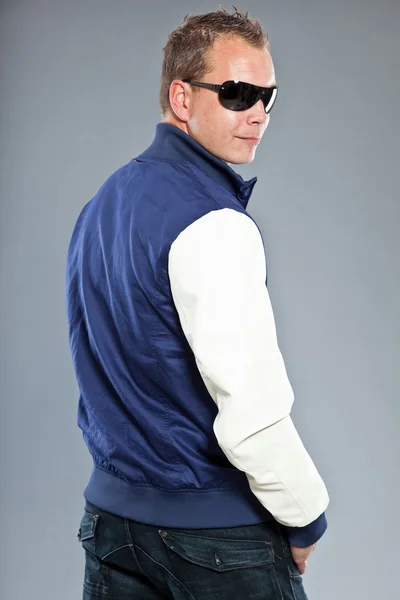 Pria muda yang bahagia dengan rambut pendek mengenakan jaket baseball biru dan celana jeans biru . — Stok Foto