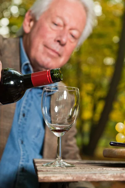 Senior man enjoying red wine outdoors in autumn forest. — Stock Photo, Image