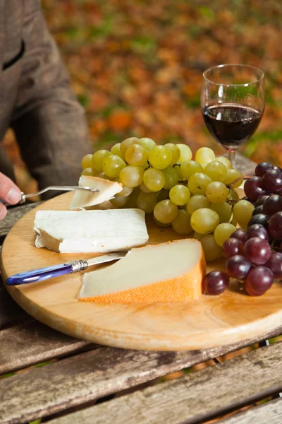 Mesa com prato de queijo, uvas e vinho tinto . — Fotografia de Stock