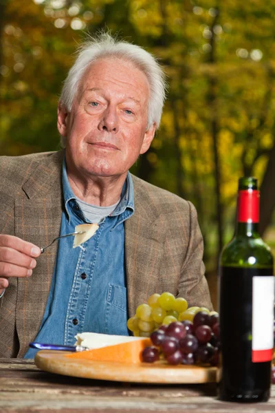 Homme âgé dégustant des raisins et du fromage en plein air dans la forêt d'automne . — Photo