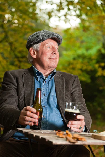 Senior man genieten van donker bier en kaas buitenshuis. — Stockfoto