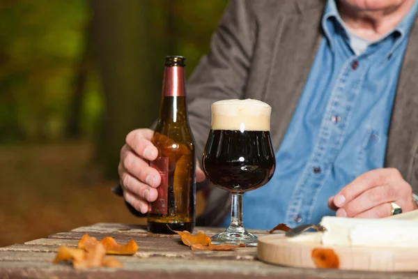Hombre mayor disfrutando de cerveza oscura y queso al aire libre . — Foto de Stock