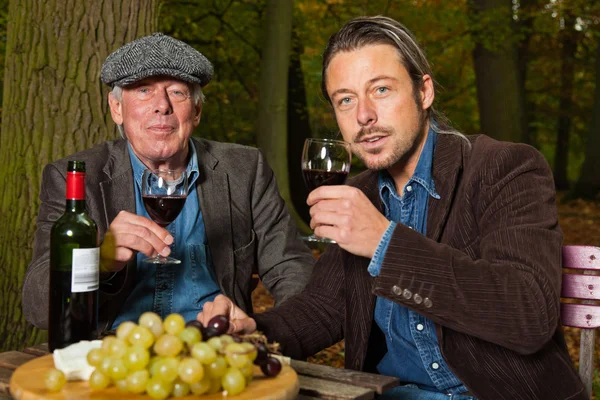 Hombre mayor y joven disfrutando de vino tinto y queso . —  Fotos de Stock