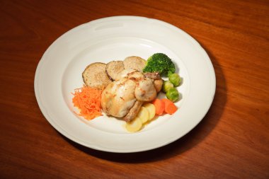 ahşap masa ve bir tabak tavuk ve sebze yemeği.