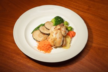 ahşap masa ve bir tabak tavuk ve sebze yemeği.