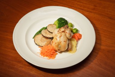 ahşap masa ve bir tabak tavuk ve sebze yemeği.