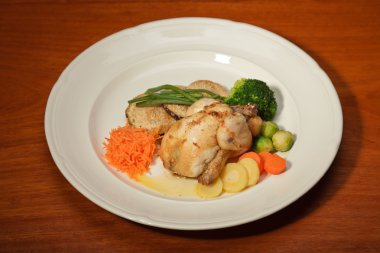 ahşap masa ve bir tabak tavuk ve sebze yemeği.