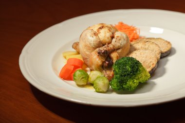 ahşap masa ve bir tabak tavuk ve sebze yemeği.