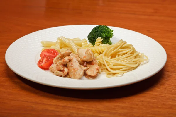 Vacsora és zöldség tészta paradicsomos csirke egy fehér lemezre és a fából készült asztal. — Stock Fotó