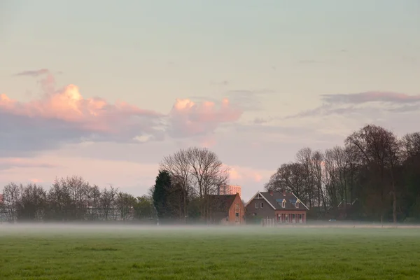 Meadow with house in the mist at sunset. Cloudy sky. Spring time. City skyline. — Stock Photo, Image