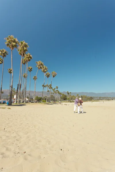 Casal caminhando na praia com palmeiras e céu azul. EUA. Califa — Fotografia de Stock