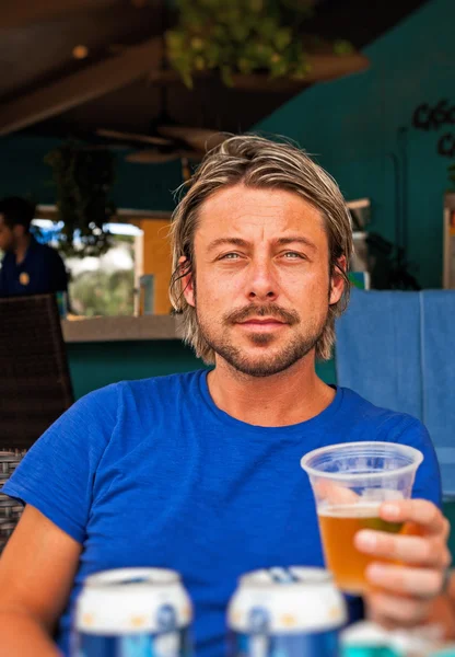 Uomo estivo con i capelli biondi che beve una birra. Camicia blu . — Foto Stock