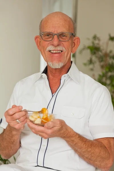 Senior Mann isst frisches Obst Gericht. Sitzen im Wohnzimmer. — Stockfoto