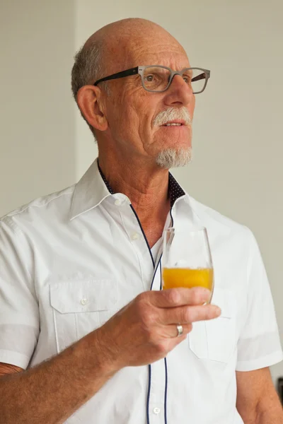 Senior mit Gläsern trinkt Orangensaft im Wohnzimmer. — Stockfoto