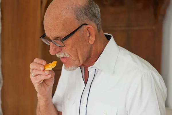 Uomo anziano che mangia frutta fresca. Seduto in soggiorno . — Foto Stock