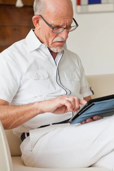 Senior man met bril met behulp van Tablet PC op Bank in de woonkamer. — Stockfoto