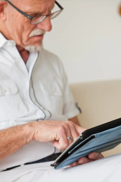 Senior man met bril met behulp van Tablet PC op Bank in de woonkamer. — Stockfoto