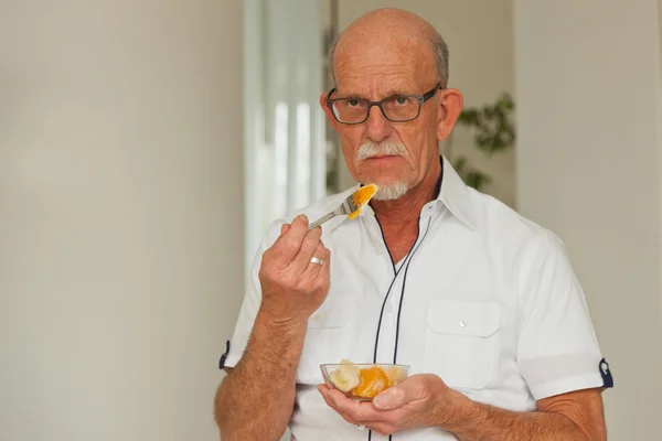 Senior man eten van verse fruitmand. vergadering in woonkamer. — Stockfoto