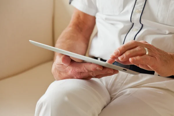 Mains de l'homme âgé utilisant une tablette. Assis sur le canapé blanc . — Photo